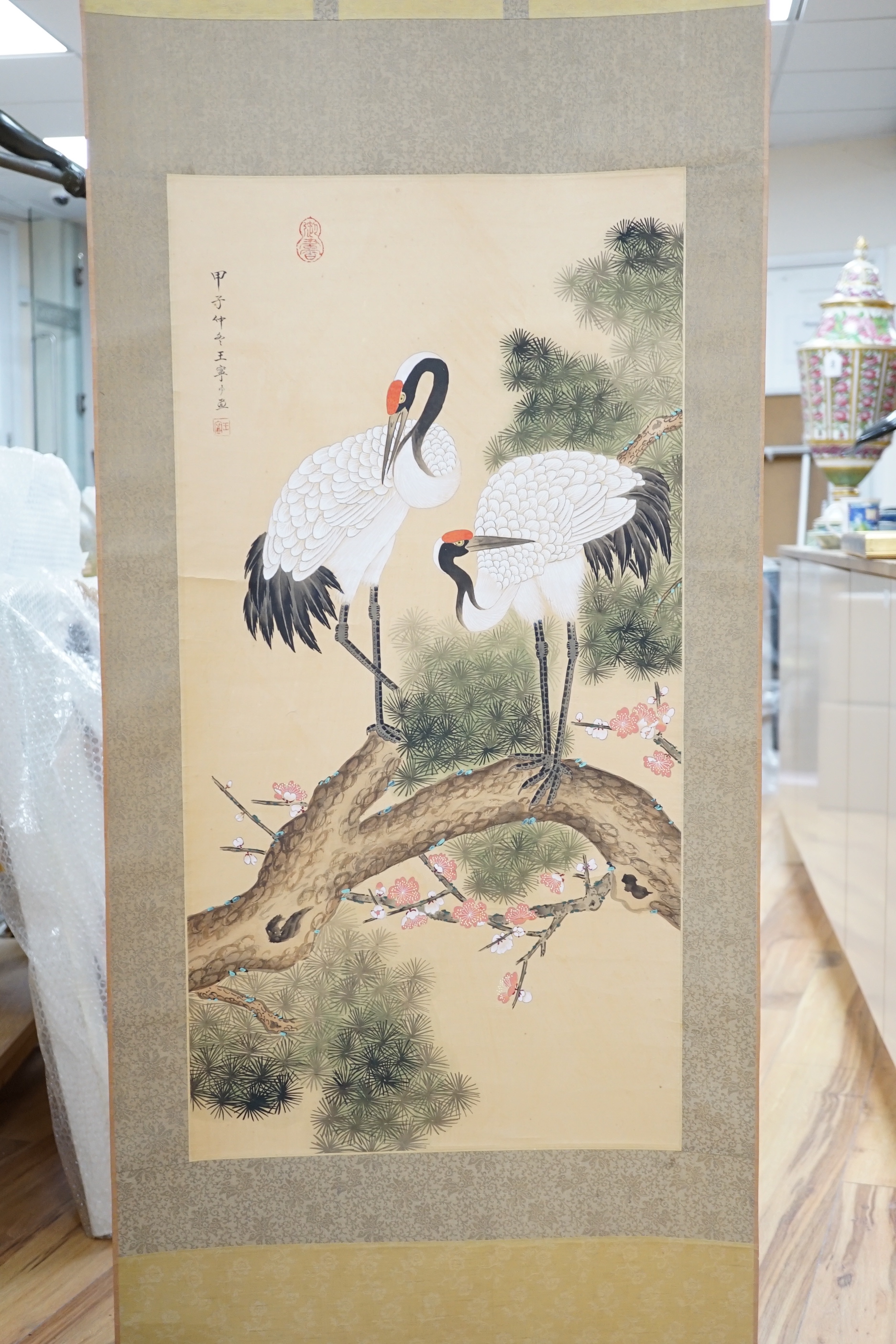 A 20th century Chinese hanging scroll watercolour on silk, two cranes on a pine tree, with brocade border, together with a blue Chinese silk table runner with brocade mon decoration